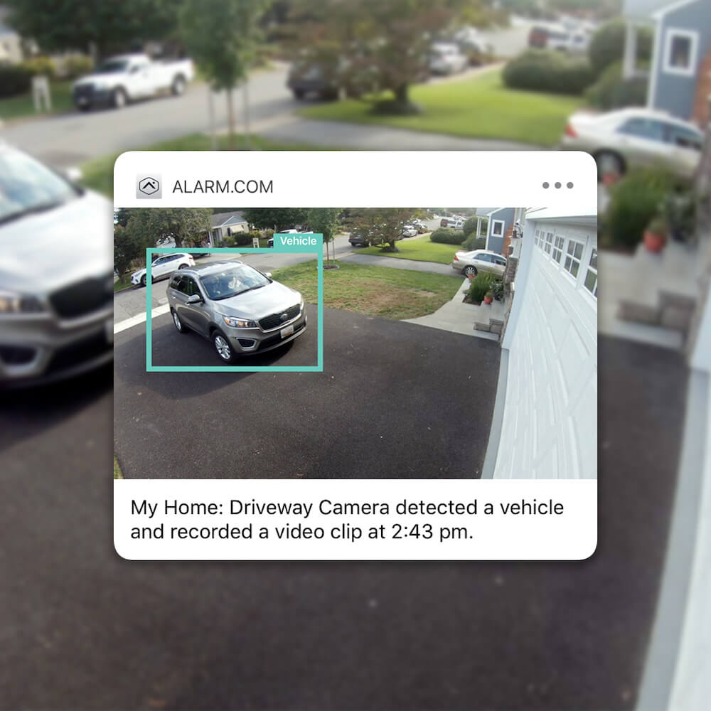 This image shows a screenshot of a security system alert from ALARM.COM, revealing a residential driveway where a camera has detected a vehicle at 2:43 pm.