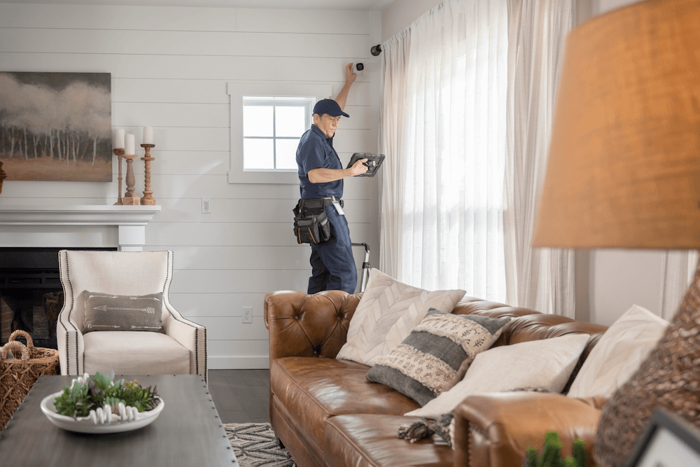 A person in a blue uniform with a tool belt is installing curtains in a well-furnished living room with a leather sofa and elegant decor.