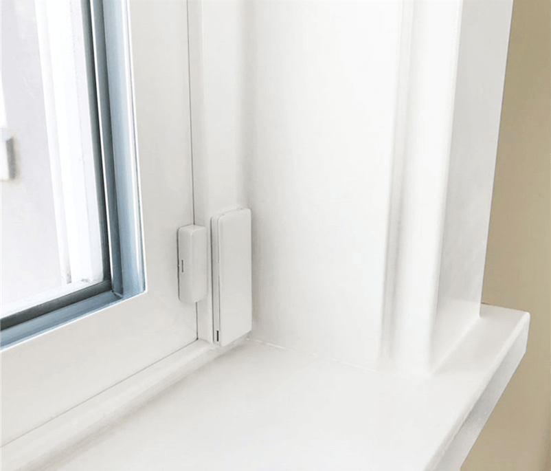 This image shows a white window frame with a closed, modern window, featuring a latch on the side, set into a cleanly painted white wall with a windowsill.