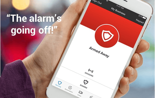 A person is holding a smartphone displaying a security alarm application with a red interface, indicating an armed status and a quote saying, "The alarm's going off!"