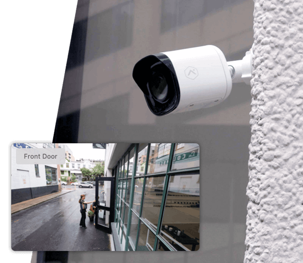 A security camera is mounted on a white wall outdoors, with an inset image showing its live feed of a person delivering a package at a storefront.