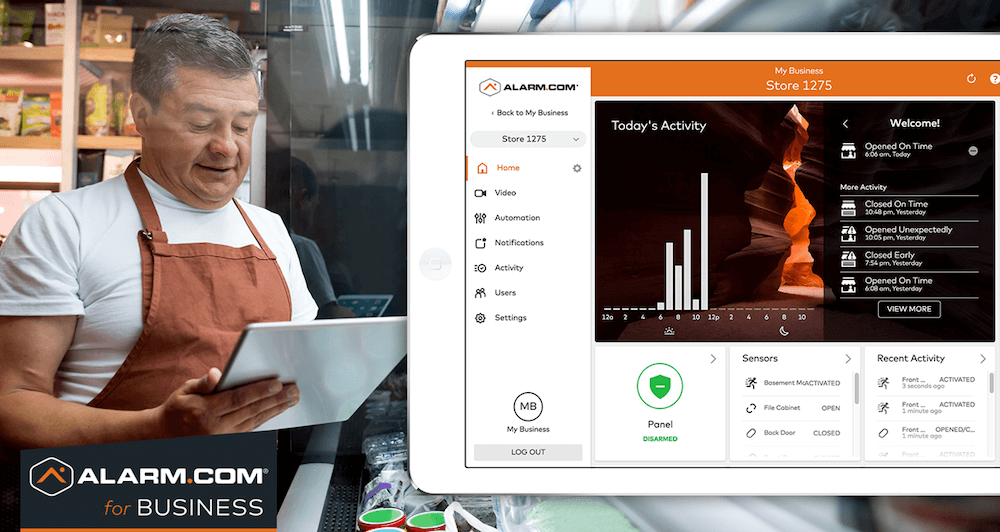 A person in a white apron smiles while using a tablet beside a visible interface of Alarm.com for Business, showing graphs and security features.