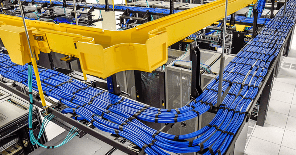 This image shows a close-up of blue network Ethernet cables organized in yellow cable management trays above a server or network racks in a data center.