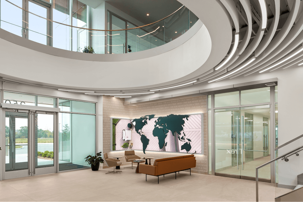 A modern lobby with a staircase, world map art, plants, contemporary furniture, large windows, and a bright, airy atmosphere.