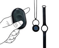 A hand holds a black oval object, likely an electronic device, next to a pendant and a wristband with similar smaller devices, possibly for tracking or synchronization.